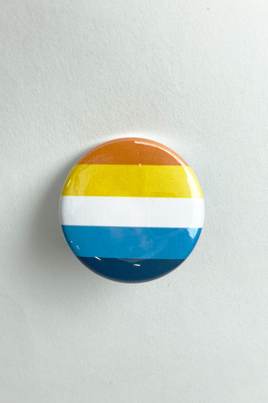 A pinback button featuring the colors of the Aroace flag.