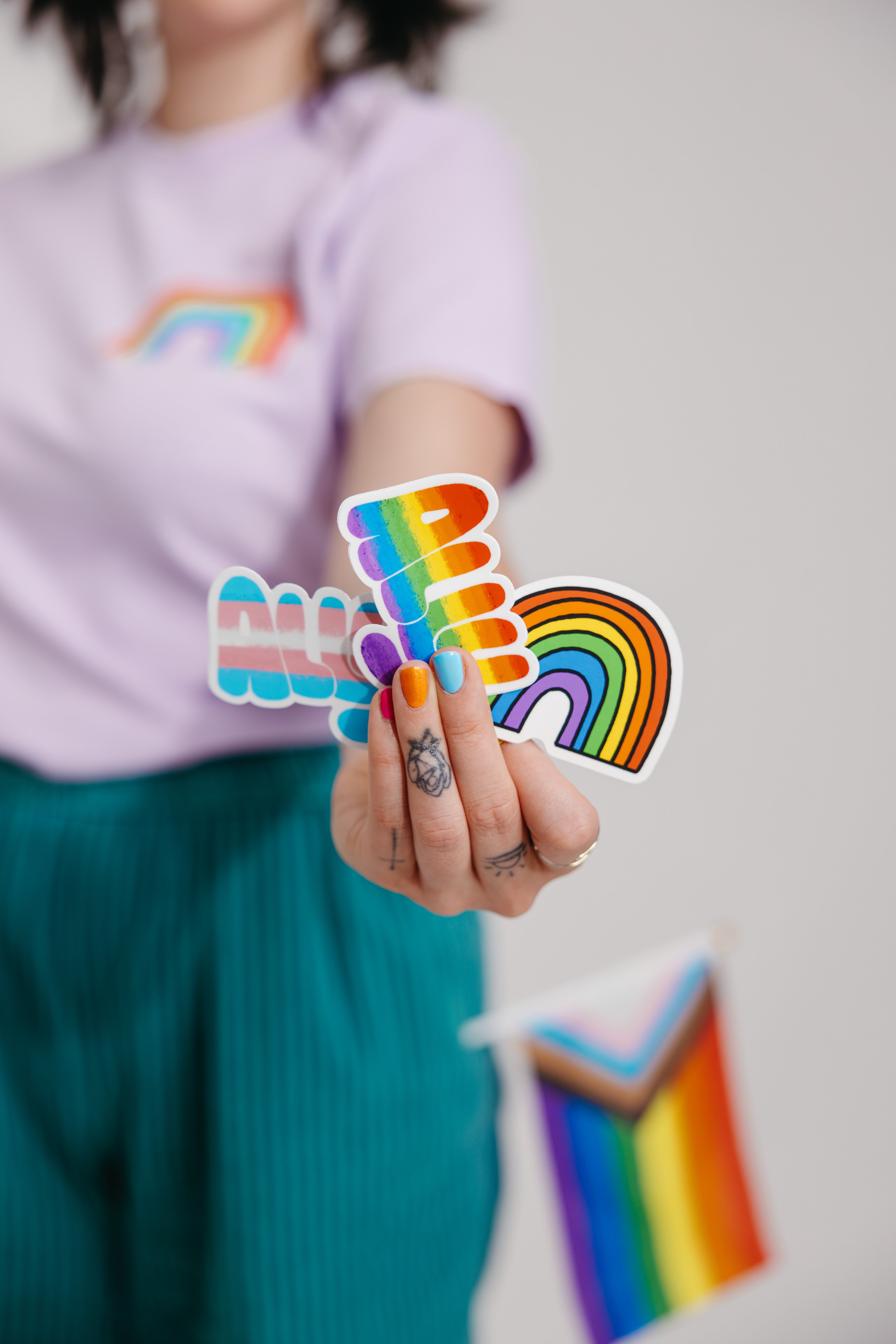 Model holding trans & gay ally stickers, wearing a Culture Flock Pride Tee