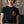 Load image into Gallery viewer, A person standing in front of a brick wall with a tapestry wearing a Black tshirt. The tshirt features an illustration of a red apple with gold stars and a green worm sticking out of it. The worm is frowning and below the apple in green text it says ROTTEN.