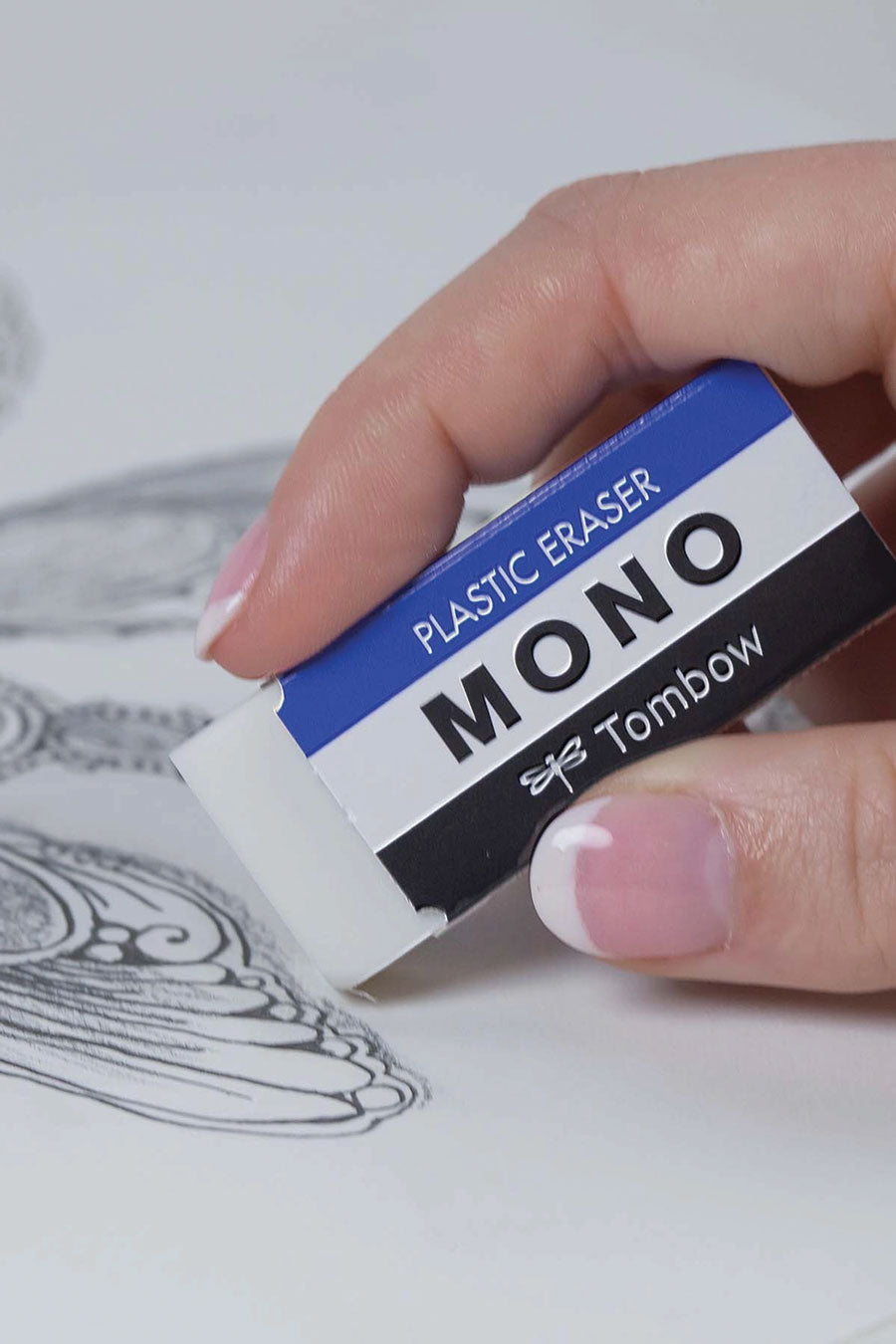 Someone using a Soft plastic eraser with a protective paper sleeve that features blue white and black stripes. The sleeve says Plastic eraser. Mono. Tombow.