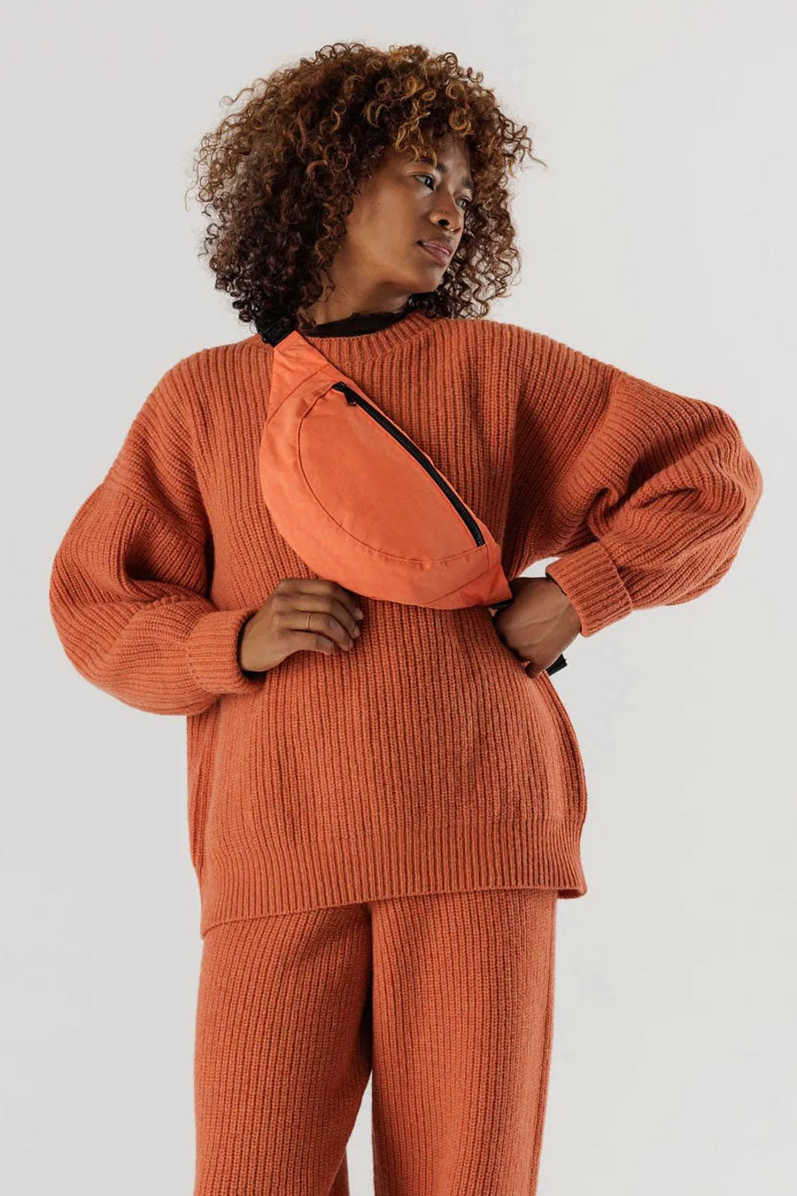 Woman wearing an orange crescent shaped fanny pack across her chest.