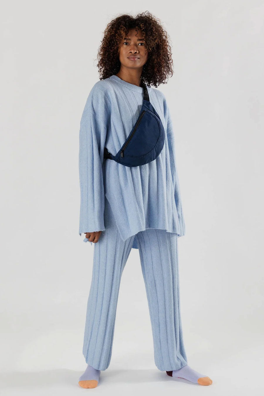 Person in blue outfit wearing Navy crescent shaped fanny pack with black straps across their chest. White background.