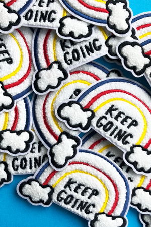Several chenille patches depicting rainbows coming out of clouds and black text reading "Keep Going" are displayed on a blue background.