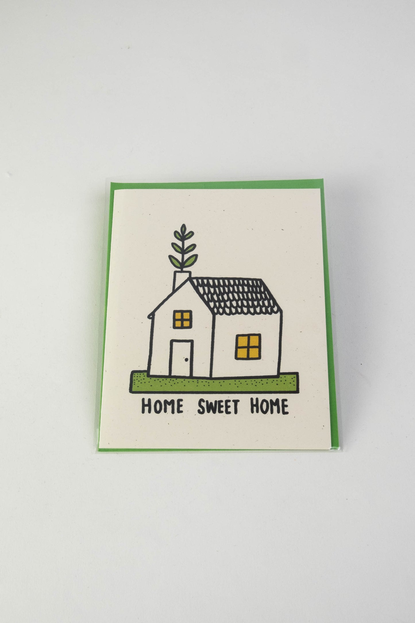 A white greeting card with the illustration of a small house with green foliage coming out of the chimney. The text along the bottom reads "Home sweet home."