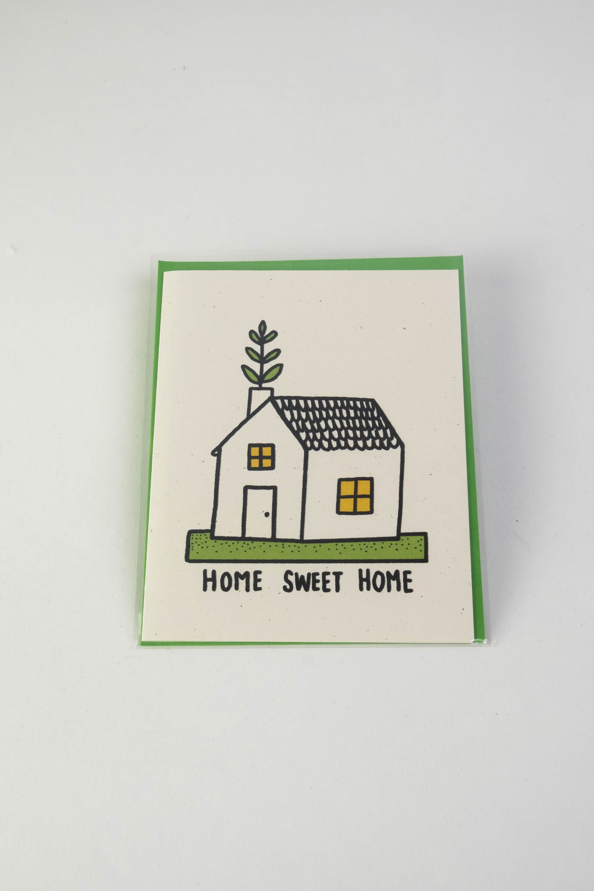 A white greeting card with the illustration of a small house with green foliage coming out of the chimney. The text along the bottom reads "Home sweet home."