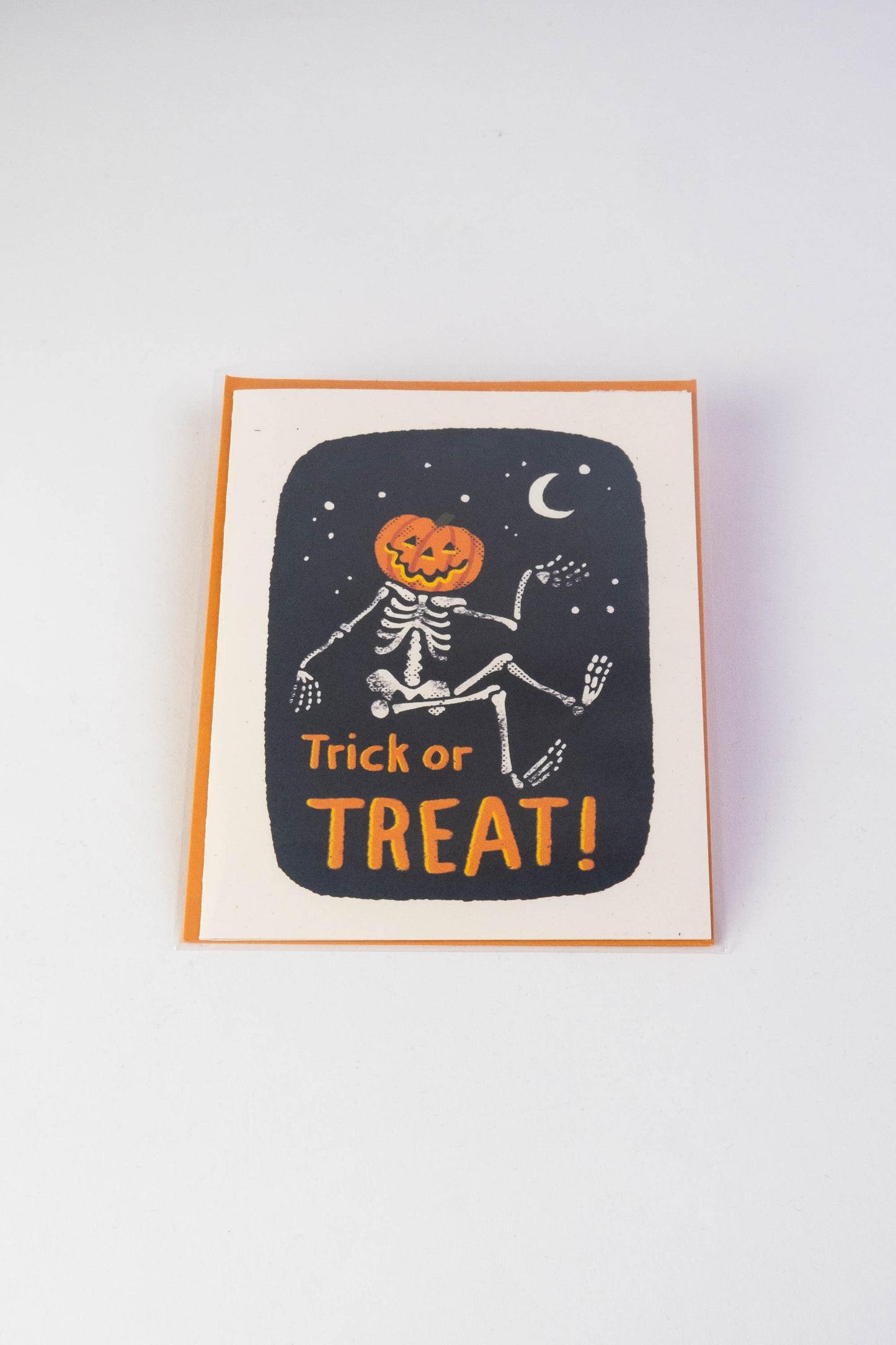 Speckletone card with orange envelope on a white background. The card features a skeleton with a jack-o-lantern head against a black stary night. Under the skeleton in orange lettering the card says Trick or Treat.