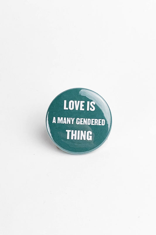Blue Green Button on a white background that says " Love is a many gendered thing" in white text.