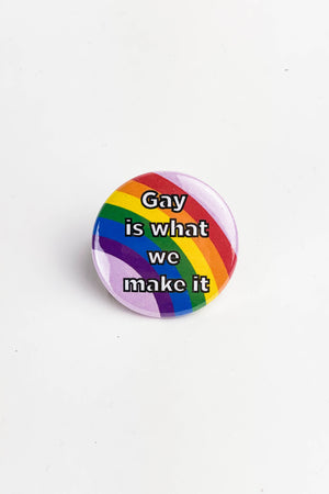A pinback button with a pink background with a rainbow. The text reads "gay is what we make it."
