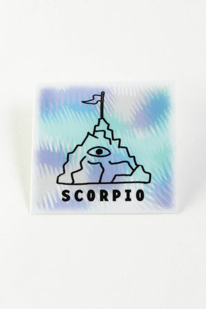A square white, teal and purple sticker with an illustrated image of a craggy mountain with an eyeball in the center and a small flag on top. The black text on the bottom reads "Scorpio."