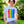 Load image into Gallery viewer, A person with dark curly hair is standing on the sidewalk in front of a lush green yard and big trees. They are wearing a white t-shirt with a vertical rainbow flag and small white rainbows overlayed. 
