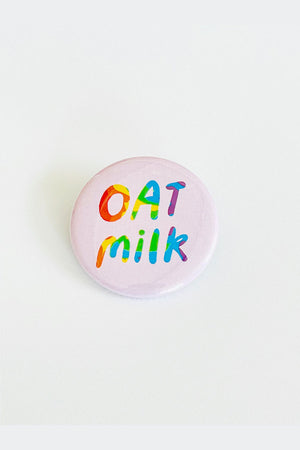 Lilac button on a white back ground. The button says Oat Milk with wavy rainbow colors. 