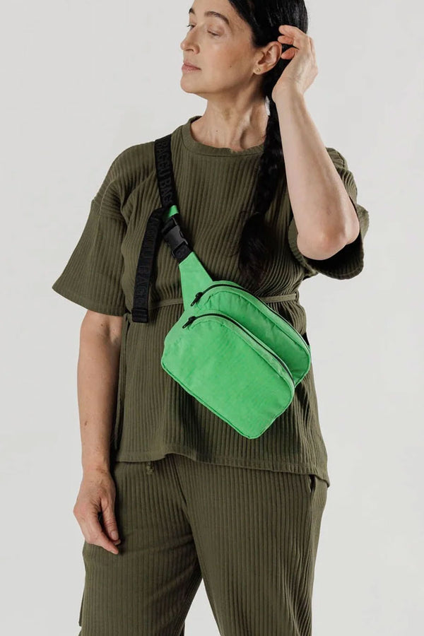 Person wearing a Nylon fanny pack with black straps and two compartments. Fanny pack is Aloe Green.