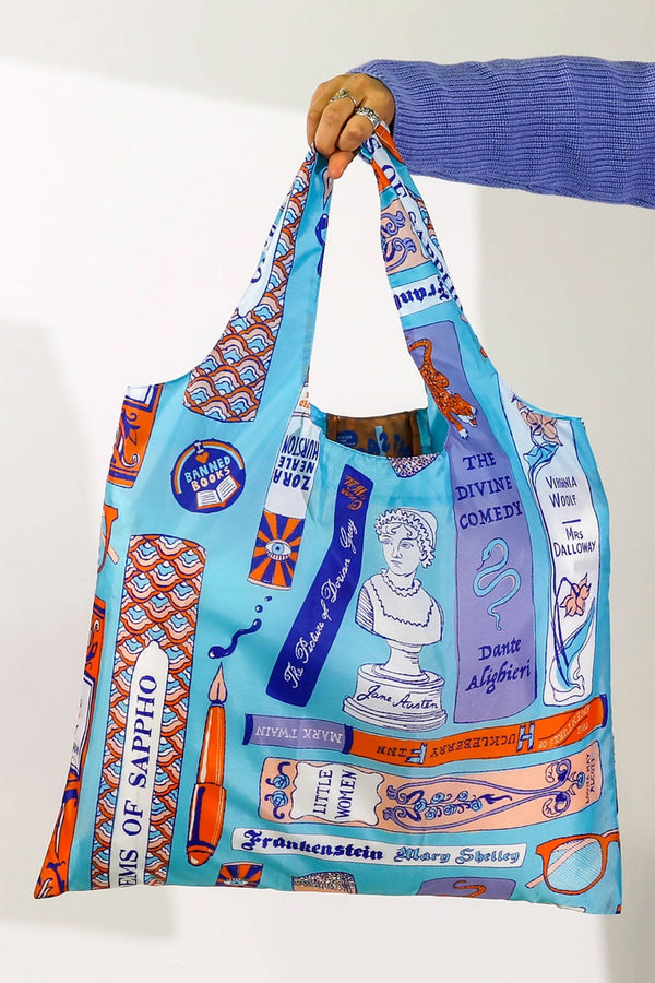 Blue reusable tote bag. The tote is covered in Book spines and covers, pens, glasses, and busts of authors.