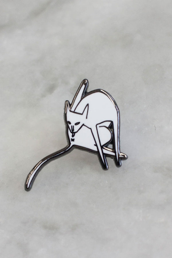 Enamel pin with a cat bathing itself . White background.