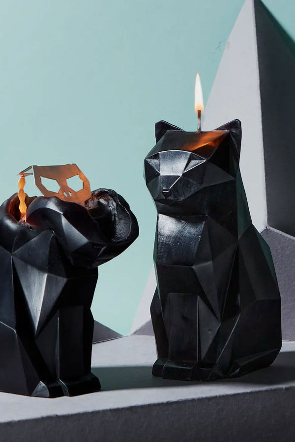 Black geometric cat shaped candles against a blue background. Once candle is lit and the other candle is slightly melted which reveals a metal skeletal frame. 