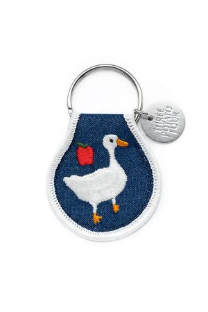 Embroidered keychain with silver hardware. Keychain features a goose with an apple on a denim background with white border.