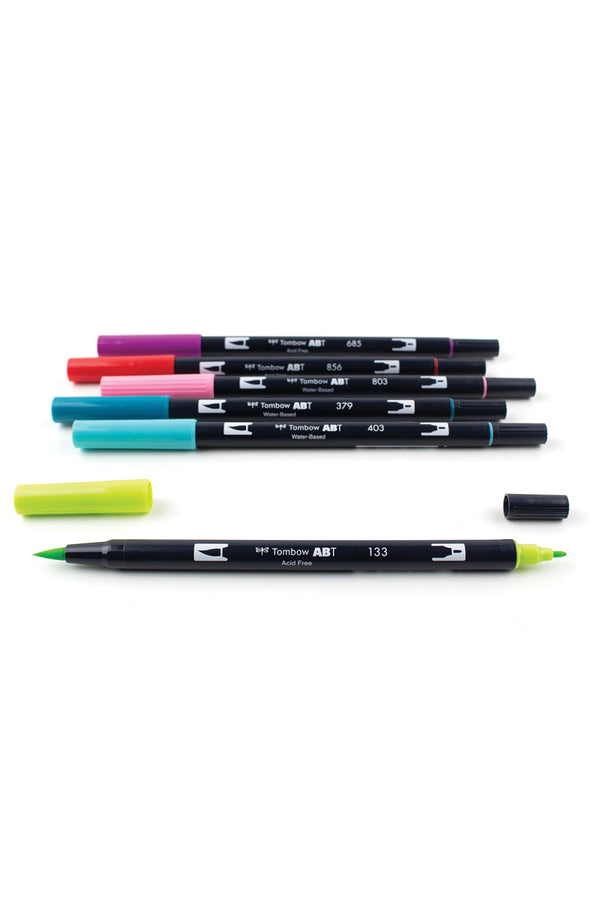 Set of 6 Dual Brush Pen colors. Flexible brush tip and fine tip in one marker. Colors Included: Chartreuse, Bright Blue, Jade Green, Pink Punch, Poppy Red, and Deep Magenta. The markers are laying on a white surface with the marker lids removed on the chartreuse marker. 