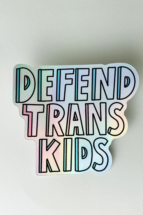 Holographic Die Cut sticker that says Defend Trans Kids in block lettering with shadow colors of blue and pink. White background.