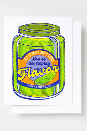 Greeting card of a jar of pickles. The label on the jar says Its not Ageing. You're developing Flavor. Happy Birthday. White background. 