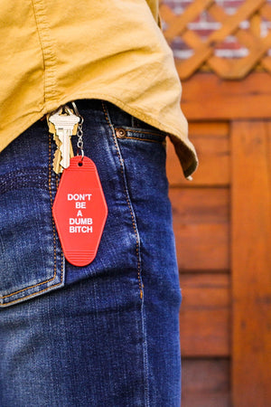 Red vintage style keychain that says Don't Be A Dumb Bitch in white text.