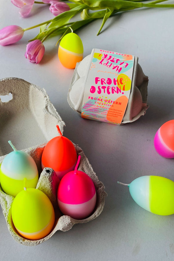 Four egg shaped candles. Each candle is dip dyed in neon colors of pink, orange, yellow, and teal. packaged in a small egg carton.