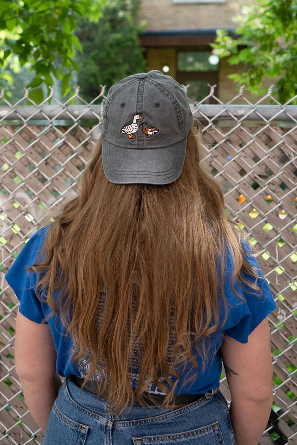 A person wearing a Faded black denim dad hat with two embroidered ducks.