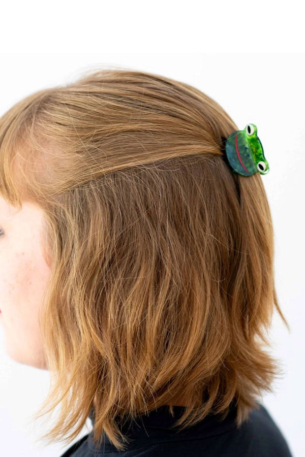 Person wearing mini green frog hair clip in their hair. White background.