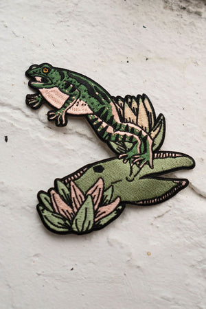 Self adhesive embroidered patch of a frog jumping off of a lily pad.