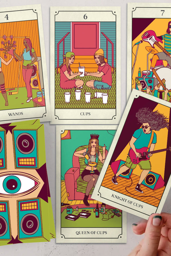 Illustrated tarot cards laid on a table. The cards depict illustrated scenes of grunge musicians.