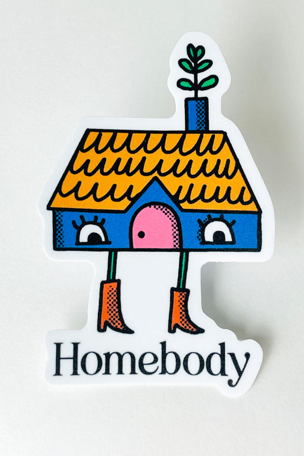Die cut sticker of a blue house with a yellow roof and a chimney. The house has a pair of eyes for windows, a pink door, and a plant coming out of the chimney. The house also has a pair of legs wearing red boots standing over text that says Homebody. White background.