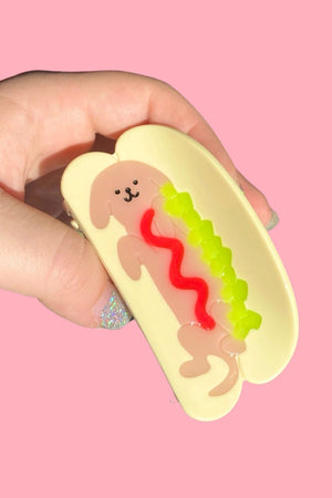 Hair clip shaped like a hot dog bun. In the middle is a dog with ketchup and relish on it to resemble a Hot Dog.
