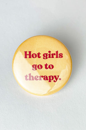 A pale yellow pinback button with red text that reads "Hot Girls Go To Therapy"