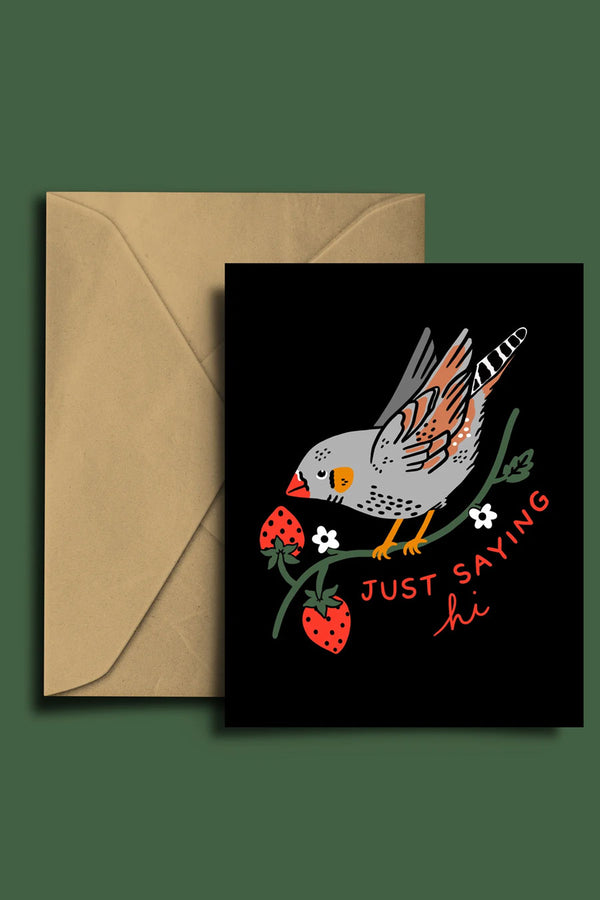 Black greeting card with kraft brown envelope against a forest green background. The card has an illustration of a finch bird on a branch with strawberries. Underneath the card says Just saying Hi in red lettering.