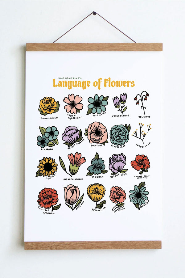 Digital print on white cardstock hanging from a wooden magnetic frame against a white wall. The print says Language of Flowers in yellow text at the top and features 16 different types of flowers. The flowers are assigned different names like Social Anxiety, Harsh Judgement, Self Doubt, and Uselessness for example. The flowers range in colors of yellow, pirnk, blue, lilac, and poppy red.