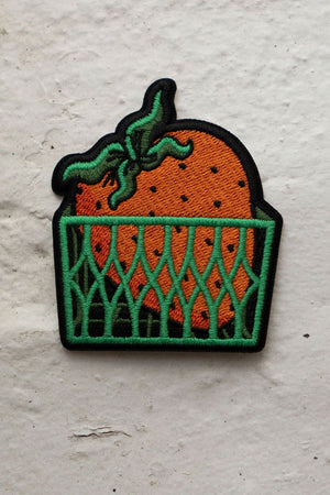 Self adhesive patch of a large strawberry in a green produce carton.