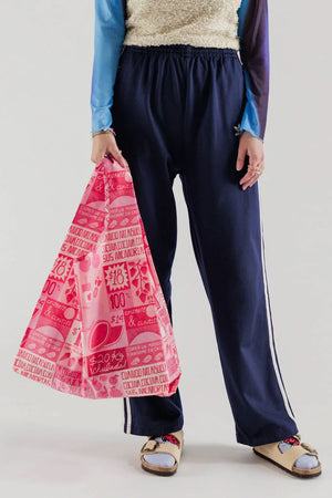 Person holding a Pink and Red reusable tote bag featuring different illustrated grocery signs inspired by Mexico City.