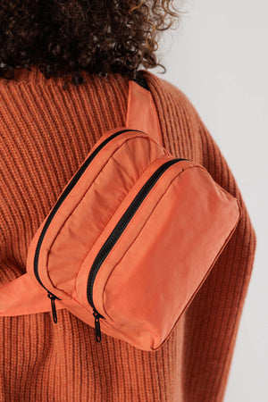A person wearing a Nylon fanny pack with two main compartments across their back. Fanny pack is bright orange with black strap.