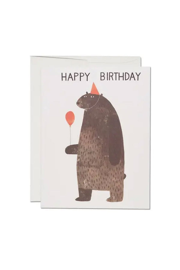 White greeting card featuring illustration of a brown bear with a red party hat and holding a red balloon. Above the bear the card says Happy Birthday. White background.