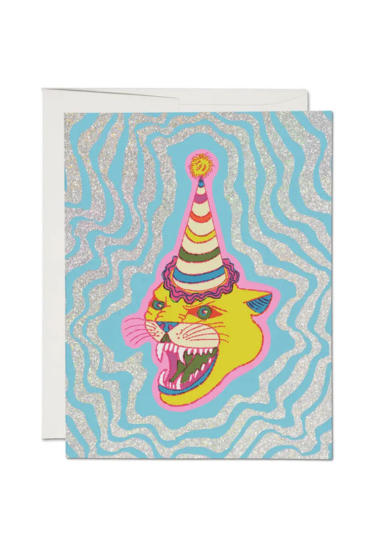 Card featuring an illustration of a yellow lioness  rawring while wearing a rainbow striped birthday party hat. Surrounding the cat, is ripples of glitter stripes out to the edge of the card. White background.