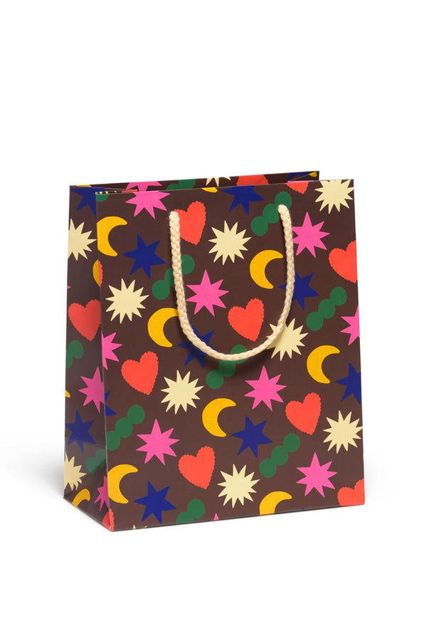 Brown Gift bag with cream color rope handle. Bag features all over print of yellow moons, red hearts, green dots, and white, blue, and pink stars.