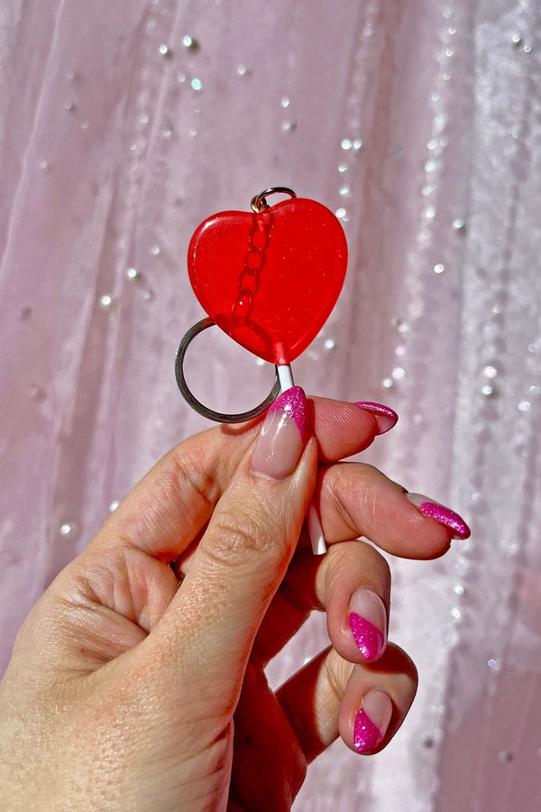 Someone holding a Red heart shaped lollipop with silver hardware.