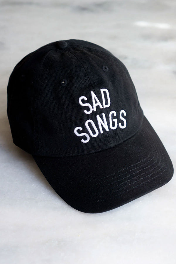 Black baseball cap that says SAD SONGS across the front in white embroidered text. White background.