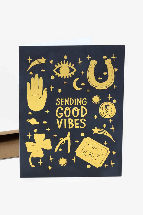 Navy greeting card with gold illustrations of lucky charms (4 leaf clover, horseshoe, penny, wishbone, shooting star) and the card says Sending Good Vibes in the center.