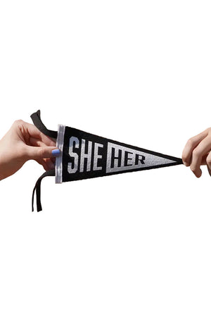Two people holding a Small black and white pennant with white edge. The first half of the pennant is black with white letting that says She. The other half of the pennant is white and in black lettering says Her. White background.