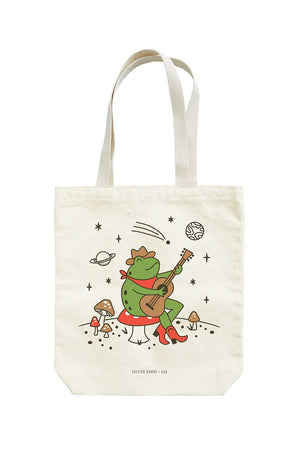 Tote bag with a frog sitting on a toadstool mushroom playing guitar underneath a starry sky with plantes and shooting stars.