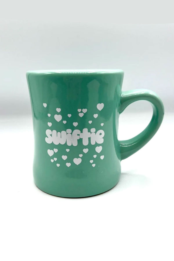 Green diner mug that says Swiftie in white bubble text and surrounded by white hearts.