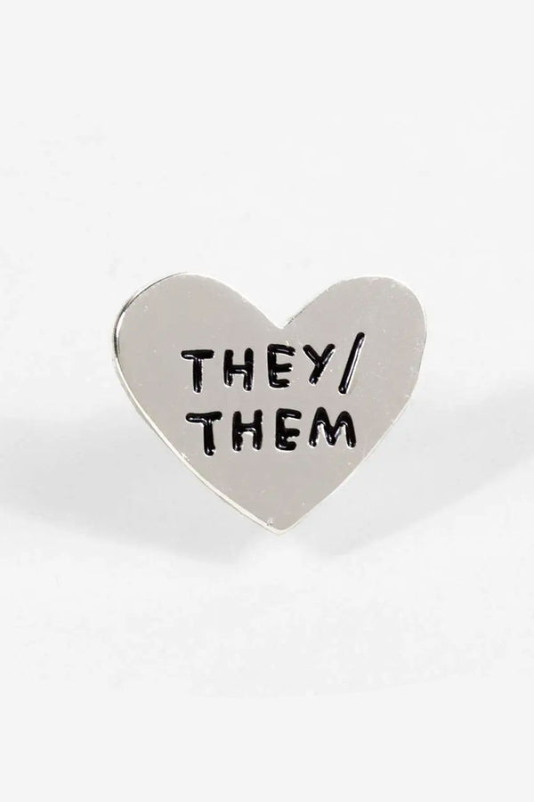 Silver heart shape enamel pin. The pin says They/Them  in black text.