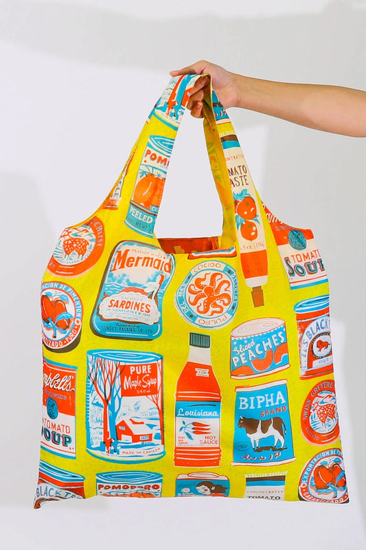 Yellow reusable tote bag covered in all over print of illustrated food products in white, red, and blue.