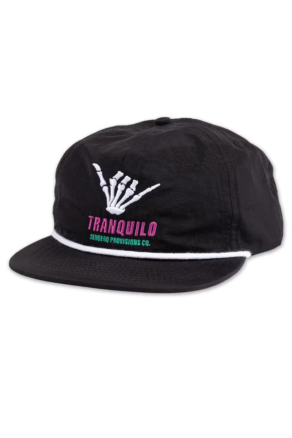 black baseball cap with white rope across the bill. The hat says Tranquilo with a skeleton hand above it doing the "Hang Loose" sign. White background.