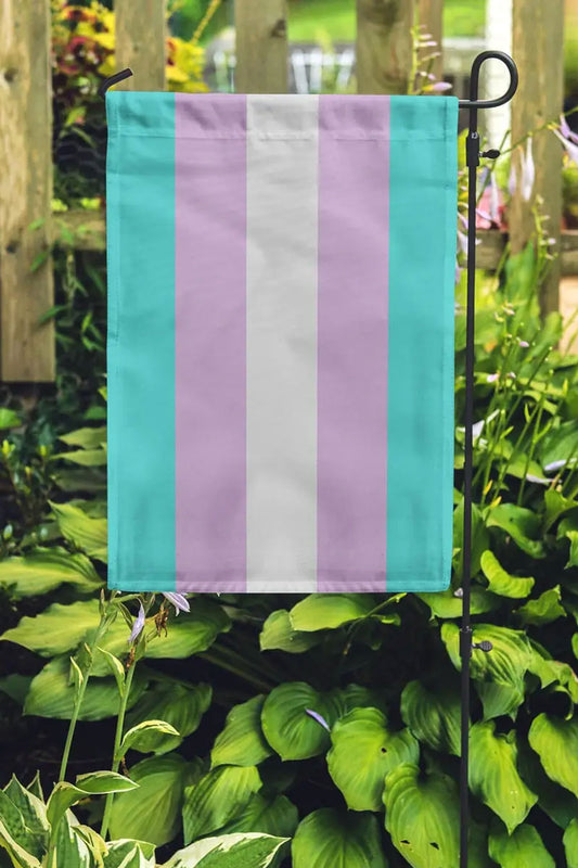 Garden flag on a pole. The flag is the Transgender Pride flag with blue, pink, and white stripes.